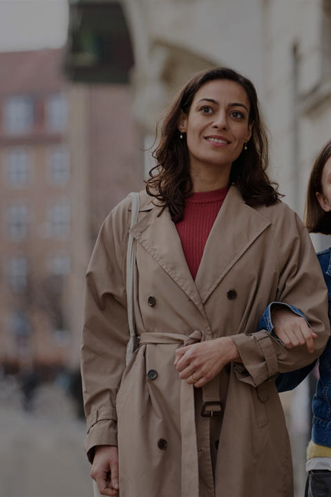A woman and young lady walk hand in hand down a street with a smart phone showing SES Family content imposed on the foreground