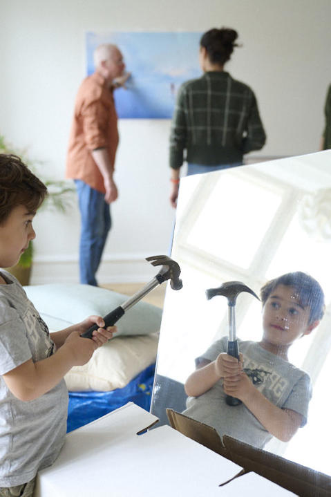 A young boy stands poised to strike a mirror with a hammer while four adults speak in the background