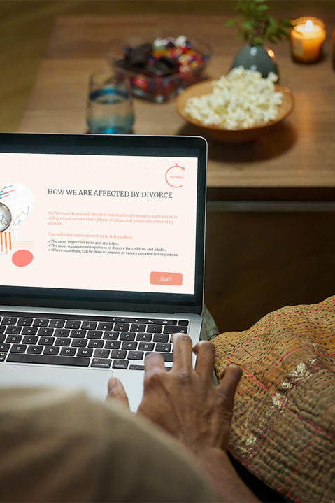 Over the shoulder view of a man sitting on a couch using the SES website with snacks on the table.