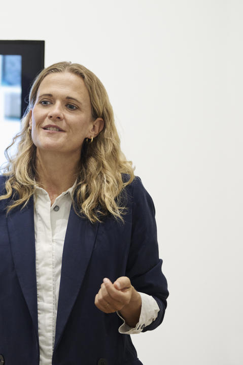 Woman giving a professional presentation in front of a screen showing a young woman looking at a tablet.