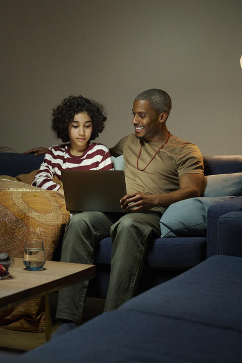 Man sitting in sofa with child, looking at a laptop together.