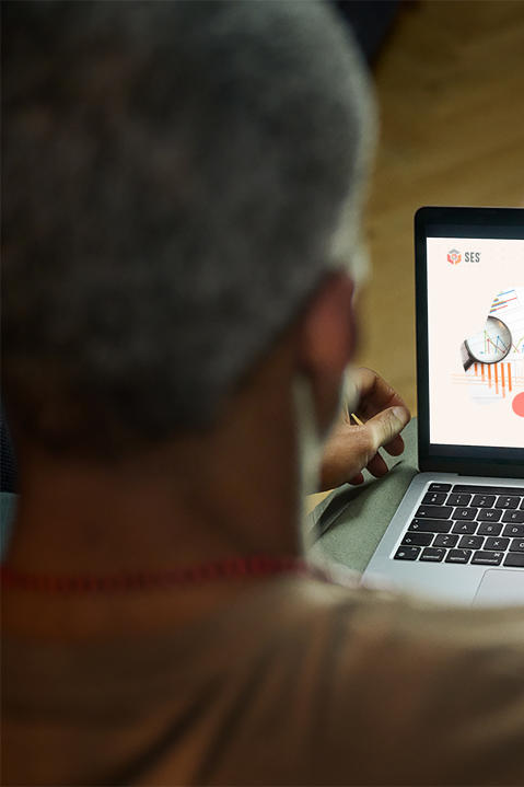Over the shoulder view of a man sitting on a couch using the SES website with snacks on the table.