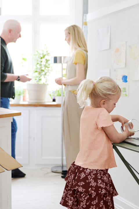 An unobserved child pours liquid onto a laptop while parents speak in the background