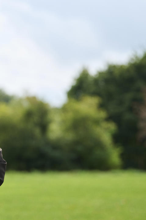 A woman stands outside in a dark professional jacket with her arms crossed